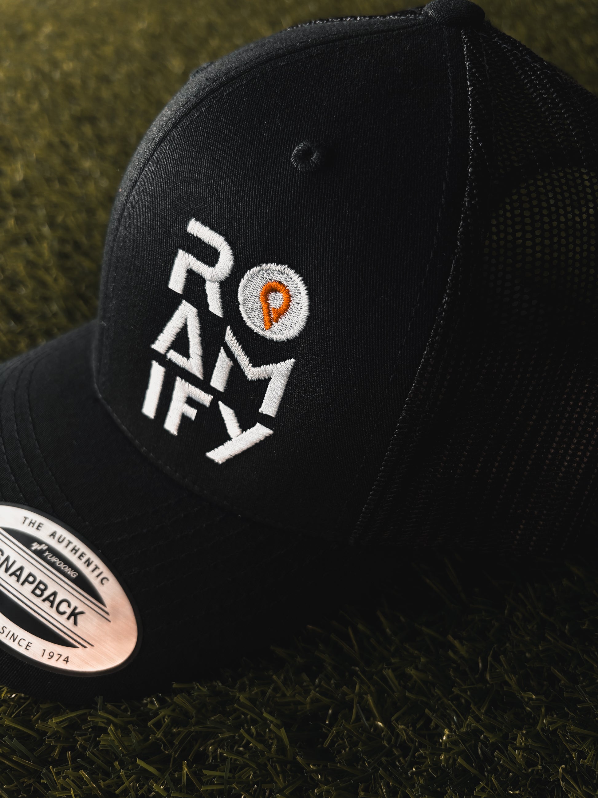Black cap with 'Roamify' logo on a grass background