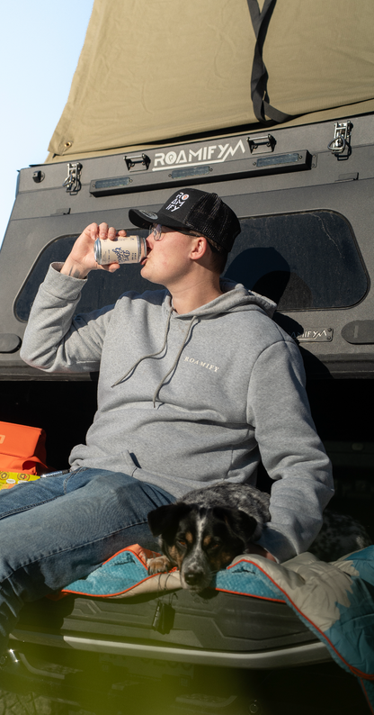 Person sitting in the back of a vehicle with a dog, drinking from a can.